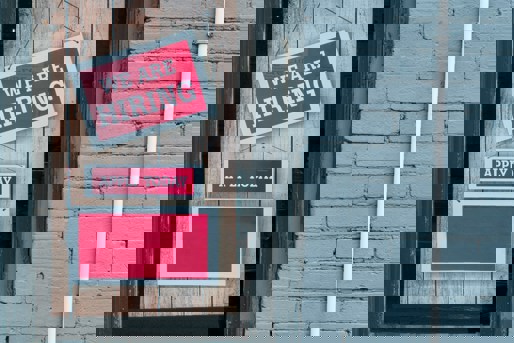 Wooden door with hanging red signs saying 'we are hiring' and 'apply today'