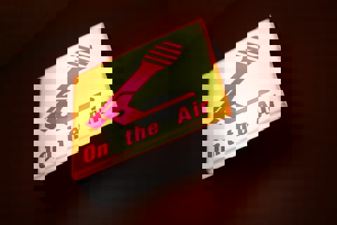 Yellow illuminated sign with an image of a microphone and wording: 'On the Air' in pink